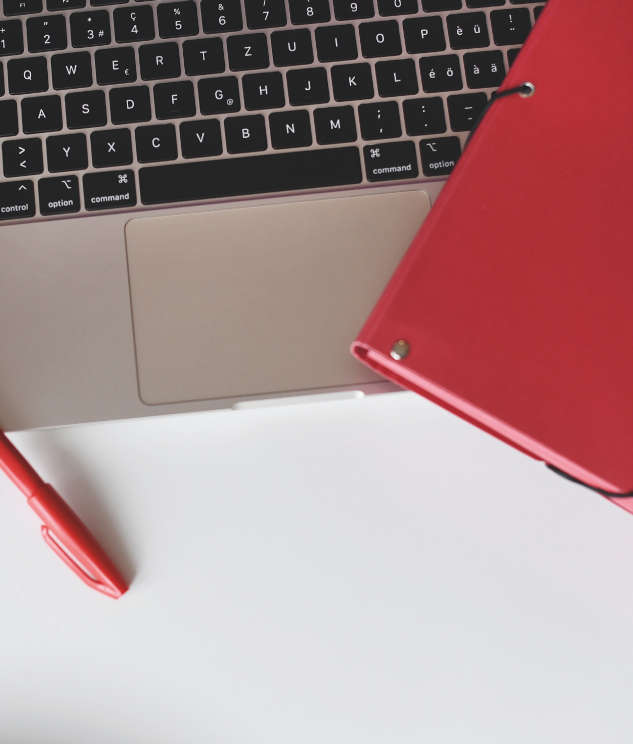 Auf einer Laptoptastatur liegt ein roter Ordner und ein roter Stift